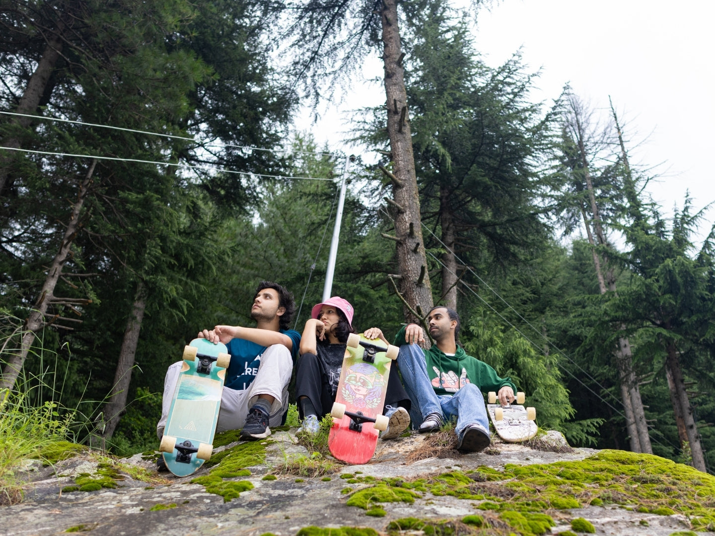 Three people sitting on a rock with skateboards in a forest setting
